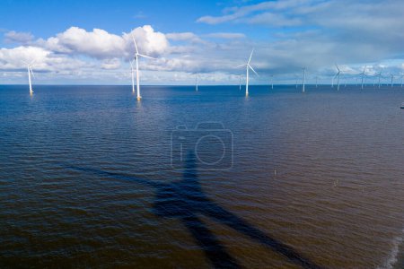 Foto de Un vasto cuerpo de agua resplandece bajo la luz del sol primaveral mientras las turbinas eólicas se mantienen altas en el fondo, aprovechando el poder del viento. turbinas de molinos de viento en el océano de los Países Bajos - Imagen libre de derechos