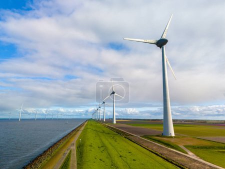 Foto de Una pintoresca escena de elegantes turbinas de viento de pie en una fila junto al océano en un dique holandés en primavera, aprovechando la energía renovable en un brillante día de primavera. en el Noordoostpolder Países Bajos - Imagen libre de derechos