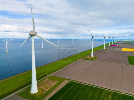 Téléchargez les photos : Une vue aérienne fascinante d'un parc éolien près de l'océan, où des pales de turbine géantes tournent gracieusement sur fond d'eau dans le polder Noordoostpolder Pays-Bas - en image libre de droit
