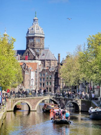 Photo for Amsterdam Netherlands 21 April 2024, A boat peacefully glides down the river, surrounded by towering buildings that create a stark urban landscape. - Royalty Free Image