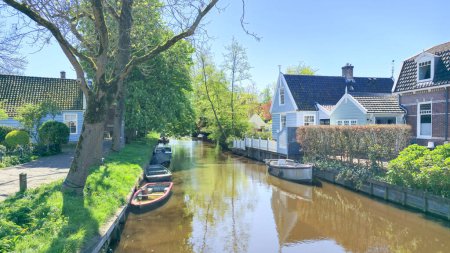 An einem ruhigen Tag gleiten die Boote gemächlich durch den ruhigen Kanal, der von charmanten Häusern gesäumt ist. Broek in Waterland Niederlande 