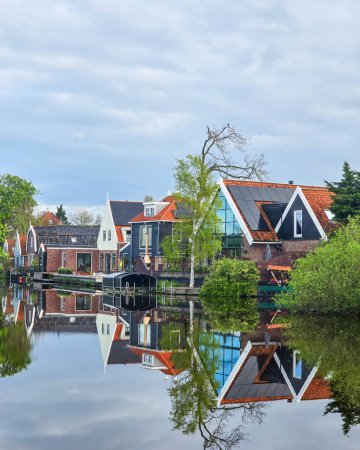 Un tranquilo cuerpo de agua enclavado entre exuberantes árboles verdes y casas encantadoras, creando una pintoresca e idílica escena de belleza natural casas antiguas en Broek en Waterland en los Países Bajos