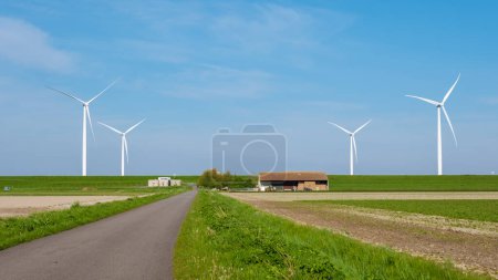 Eine malerische Straße schlängelt sich durch ein riesiges Feld, im Hintergrund turmhohe Windräder. Die Turbinen drehen sich anmutig im Wind und nutzen erneuerbare Energien im Noordoostpolder Niederlande