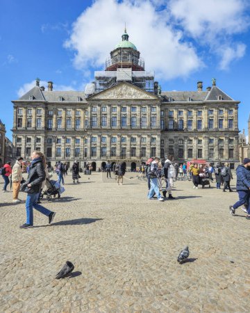 Foto de Ámsterdam Países Bajos 21 abril 2024, Un grupo diverso de personas explorando el gran edificio de arquitectura, admirando sus intrincados detalles y charlando animadamente mientras pasean por la plaza Dam - Imagen libre de derechos