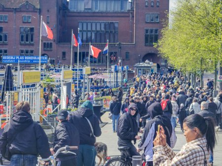 Foto de Ámsterdam Países Bajos 21 abril 2024, Una vibrante escena se desarrolla como un gran grupo de personas, procedentes de diversos orígenes, atraviesan una animada calle urbana - Imagen libre de derechos