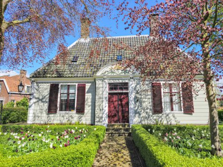 Photo for Broek in Waterlands Netherlands 21 April 2024, A stunning white house adorned with vibrant red shutters and a welcoming red door stands out against a serene backdrop. dutch farmhouse - Royalty Free Image