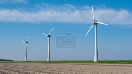 Foto de Una hilera de elegantes turbinas eólicas se alza en un vasto campo en Flevoland, Holanda, aprovechando la potencia del viento para generar energía renovable. - Imagen libre de derechos