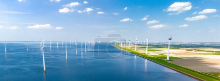 Foto de Una impresionante escena de grandes turbinas de molino de viento de pie alrededor de un sereno cuerpo de agua en Flevoland, Países Bajos. - Imagen libre de derechos