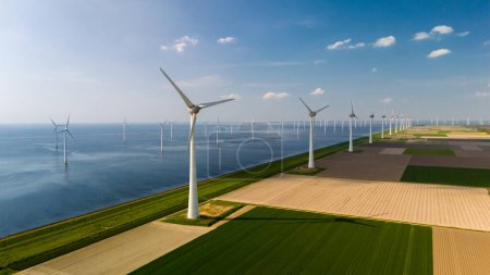 A line of wind turbines gracefully turning in the breeze beside a vast expanse of water, creating a harmonious blend of nature and technology.