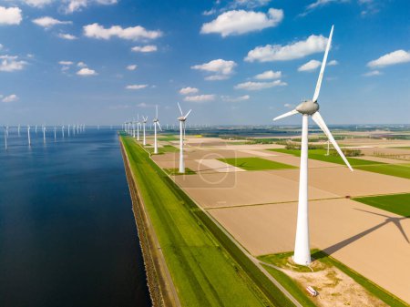 A mesmerizing landscape of wind turbines gracefully spinning in a wind farm by a serene body of water, showcasing sustainable energy production. Noordoostpolder Netherlands