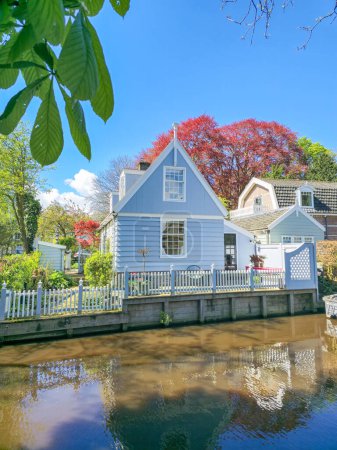 Ein charmantes blaues Haus ruht friedlich am Flussufer, umgeben von ruhigen Gewässern und heiterer natürlicher Schönheit. Broek in Waterland Niederlande 
