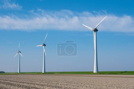 Foto de Una escena fascinante se desarrolla como una fila de imponentes turbinas eólicas que aprovechan con gracia el poder del viento en los vastos campos de Flevoland, Países Bajos. - Imagen libre de derechos