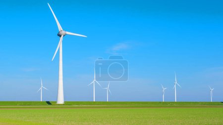 Téléchargez les photos : Vue panoramique d'un parc éolien aux Pays-Bas Flevoland, avec plusieurs moulins à vent tournant gracieusement en arrière-plan dans un ciel dégagé. terres agricoles vertes avec éoliennes - en image libre de droit