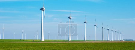Photo for Row of sleek wind turbines spinning gracefully in a vast green field, harnessing the power of the wind to generate clean energy. banner of windmill turbines - Royalty Free Image