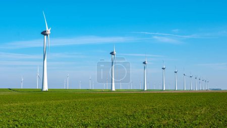 Foto de Una sinfonía de aerogeneradores de pie en un exuberante campo verde en los Países Bajos, Flevoland. enormes turbinas de molinos de viento en un campo agrícola con un cielo azul, transición energética - Imagen libre de derechos