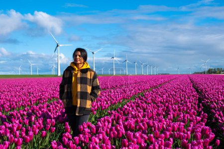 Foto de Una mujer está de pie con gracia en un vasto campo de tulipanes púrpura, rodeado por la belleza de la primavera en los Países Bajos. - Imagen libre de derechos
