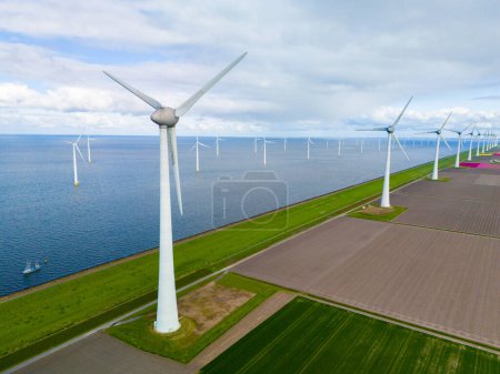 Una vista fascinante de una fila de elegantes turbinas de viento blanco en pleno movimiento, frente a los vibrantes paisajes verdes de los Países Bajos en primavera. turbinas de molinos de viento en el mar y en tierra