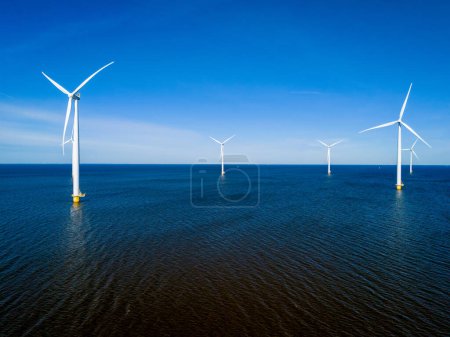 Téléchargez les photos : Un groupe d'éoliennes tourne gracieusement au-dessus de la surface de l'océan aux Pays-Bas Flevoland pendant la saison vibrante du printemps. drone vue aérienne des éoliennes énergie verte - en image libre de droit