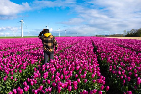 Selbstbewusst steht eine Frau an einem sonnigen Frühlingstag inmitten eines pulsierenden Meeres aus lila Tulpen auf einem holländischen Feld. Asiatische Frauen in einem Tulpenfeld in den Niederlanden