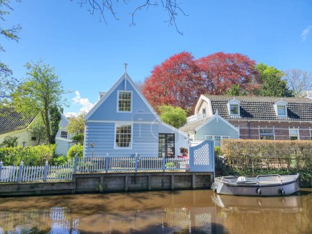 A quaint blue house peacefully sits beside a calm body of water, surrounded by a tranquil and picturesque setting. Broek in Waterland Netherlands 