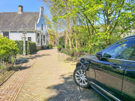 Téléchargez les photos : Une voiture électrique EV est élégamment garée devant une maison de charme, contrastant avec le moderne et le traditionnel aux Pays-Bas - en image libre de droit