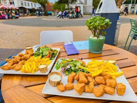 Two plates of golden-battered fish and crispy chips laid out on a rustic wooden table by the sea on Texel island.