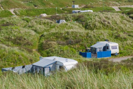 A serene scene where a group of RVs are peacefully parked on a grassy hillside in Texel, Netherlands, blending harmoniously with the natural beauty surrounding them.