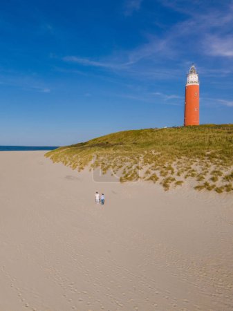 A majestic lighthouse stands tall on a sandy beach, guiding ships safely to shore with its bright beacon of light against the backdrop of the sea.