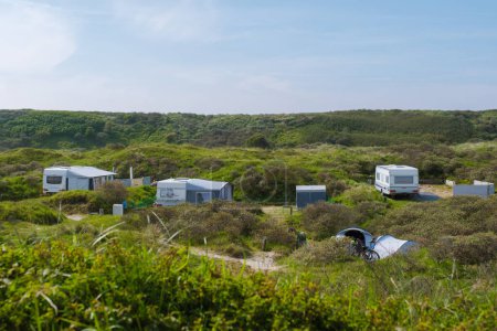Photo for A serene scene of multiple RVs parked in a lush grassy area on the picturesque island of Texel, creating a cozy camping community under the open sky. - Royalty Free Image