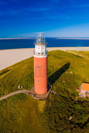 A majestic lighthouse stands tall against the shoreline, overlooking the vast expanse of the beach below. The iconic red lighthouse of Texel Netherlands