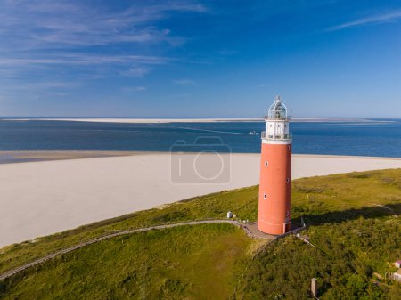 An aerial view captures a majestic lighthouse perched on a sandy beach in Texel, Netherlands, providing a guiding light to ships at sea.