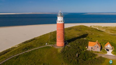 Atemberaubende Luftaufnahme eines hoch aufragenden Leuchtturms an der Sandküste von Texel, Niederlande, der Schiffe sicher an Land bringt.