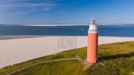 A majestic lighthouse stands tall on a sandy beach, guiding ships to safety with its bright beacon against the blue sea and sky.