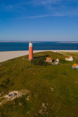 An aerial perspective of a majestic lighthouse standing tall on the sandy shores of Texel, Netherlands, overlooking the vast expanse of the sea.