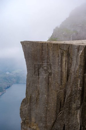 A breathtaking view from the edge of Preikestolen, a cliff in Norway. The misty landscape creates a sense of mystery and grandeur.