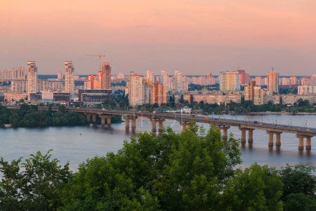 Foto de Kiev, Ucrania - 2 de junio de 2014: Esta foto muestra el puente Paton sobre el río Dniéper al atardecer, con nuevos edificios en el fondo. Los colores contrastantes de la puesta del sol y la arquitectura moderna hacen que una escena visualmente impresionante, la captura de la ciudad - Imagen libre de derechos