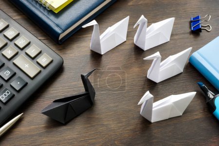 Téléchargez les photos : A Paper black swan and white ones on the office table as unpredictable events theory concept. - en image libre de droit