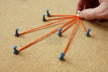The pins are connected by thread and the hand holds the main one. Delegating and leadership concept.