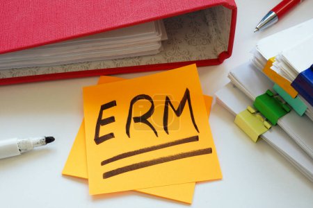 Una nota adhesiva ERM Enterprise Risk Management con una abreviatura junto a un montón de papeles.