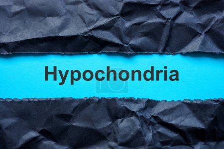 Zerrissenes schwarzes Papier und Wort Hypochondrie auf blauer Oberfläche.