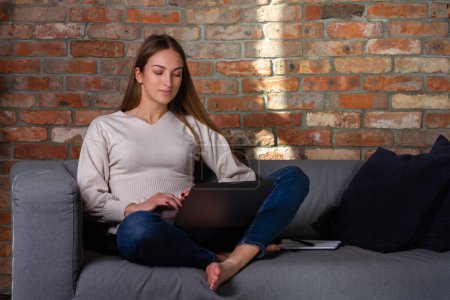 Téléchargez les photos : Femme dans un pull blanc tenant un ordinateur portable sur ses genoux et un cahier sur son côté - en image libre de droit