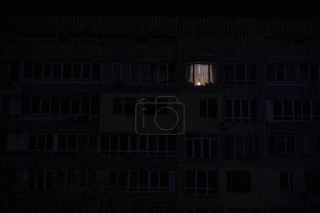 Photo for Light in one window in apartment multistorey building during the rolling blackout of electricity in a residential area of Kyiv after russian shelling - Royalty Free Image