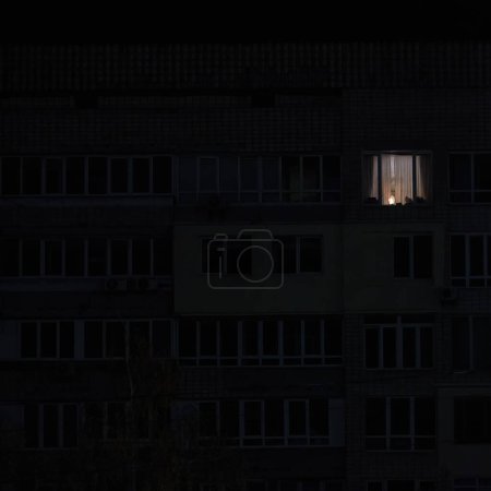 Photo for Light in one window in apartment multistorey building during the rolling blackout of electricity in a residential area of Kyiv after russian shelling - Royalty Free Image