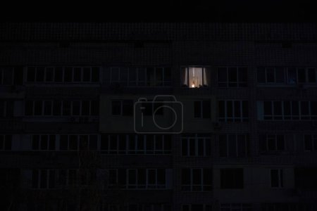 Foto de Luz en una ventana en el edificio de apartamentos de varios pisos durante el apagón de la electricidad en una zona residencial de Kiev después de bombardeos rusos - Imagen libre de derechos