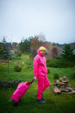 Téléchargez les photos : Homme rose posant en extérieur en costume de sport rose avec sac à roulettes. - en image libre de droit