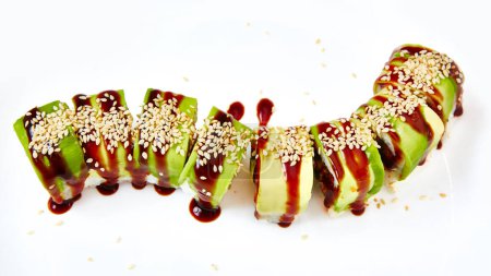 Foto de Rollo de sushi uramaki con unagi de anguila ahumada cubierto de aguacate y semillas de sésamo sobre fondo blanco. - Imagen libre de derechos