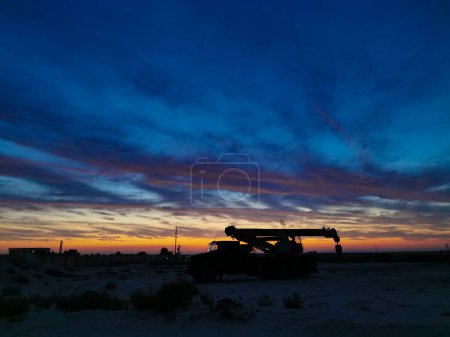 Téléchargez les photos : Silhouette d'un camion Boom dans le champ pétrolifère au coucher du soleil. - en image libre de droit
