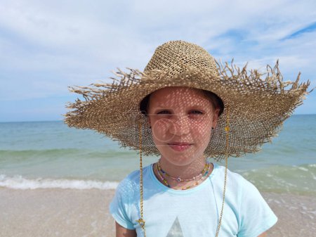Téléchargez les photos : Portrait de jeune fille mignonne en chapeau de paille sur la plage le jour ensoleillé d'été - en image libre de droit