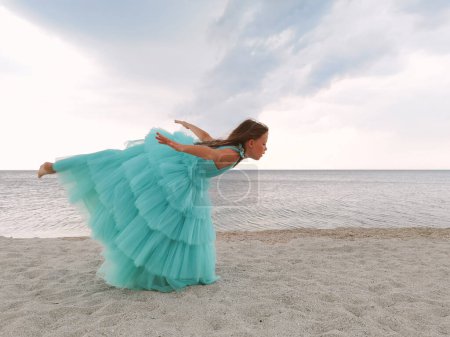 Photo for Little girl in mint dress is jumping on the beach - Royalty Free Image