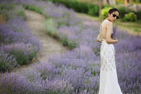Photo for Half turn woman in blooming lavender field looking at sunset. Caucasian female with her back at summer evening. Beauty concept. - Royalty Free Image